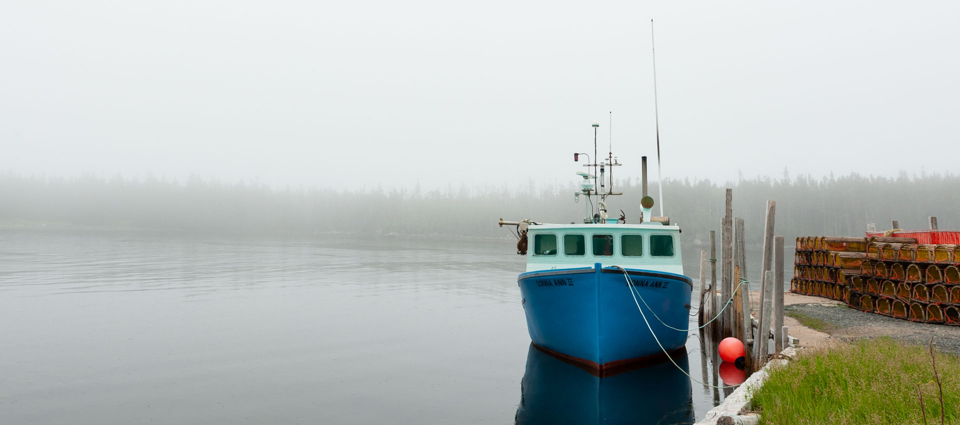 A lobster boat in the fog, tied up at a wharf with lobster traps piled alongside